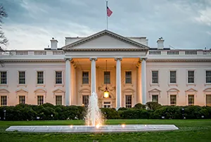 Banner illustration showing the White House supporting the U.S. coal industry with federal funding. A government building is depicted directing money toward coal-fired power plants, mining trucks, and industrial infrastructure, representing the $700 million investment announced under the Defense Production Act, including power plant upgrades, export terminal support, and new coal energy projects in multiple states.
